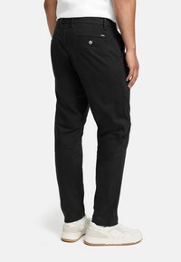 Black chinos with a straight cut, featuring a rear pocket with button closure and subtle branding. Pairing with white sneakers.