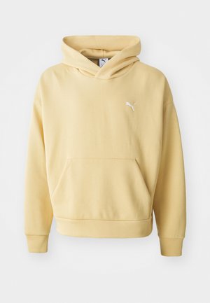 Žltá mikina s kapucňou vyrobená z mäkkej látky, so predným kangaroo vreckom a bielym logom na hrudi. Obsahuje kapucňu s nastaviteľným šnúrkovým uzáverom.