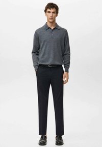 Polo grigia a maniche lunghe con colletto, abbinata a pantaloni scuri aderenti e mocassini neri. Design minimalista e texture liscia.