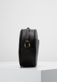 Černá kabelka přes tělo z hladké kůže s kulatým tvarem, vybavená tenkým nastavitelným popruhem a detaily v barvě zlata na přezce.