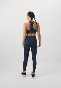 Un reggiseno sportivo blu scuro e leggings abbinati presentano un motivo a vortice. Il materiale è elasticizzato e aderente, con un design a schiena scoperta.