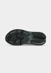 Μαύρη και γκρι σόλα παπουτσιού New Balance με σχεδιασμένο πέλμα και κυρτές αυλακώσεις για πρόσφυση, εμφανίζεται επίπεδη σε απλό ανοιχτό φόντο.