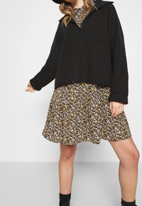 Black chunky knit sweater with a zip collar layered over a floral patterned dress featuring small white, yellow, and orange flowers on a dark background.