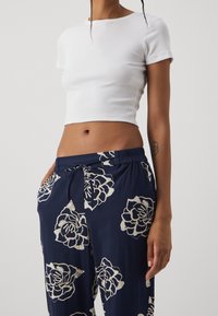 White ribbed crop top with short sleeves, paired with navy pants featuring white floral patterns and an elastic waistband.