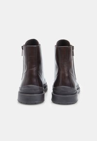Botas de cuero marrón hasta el tobillo con cremalleras verticales en la parte trasera, parte superior texturizada, punta redondeada y suelas de goma negra para mayor agarre.