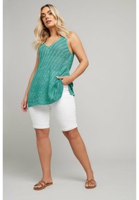 Teal stickad linne med V-ringning, med sid slits, parat med vita bermudashorts och bruna sandaler med dekorativa detaljer.