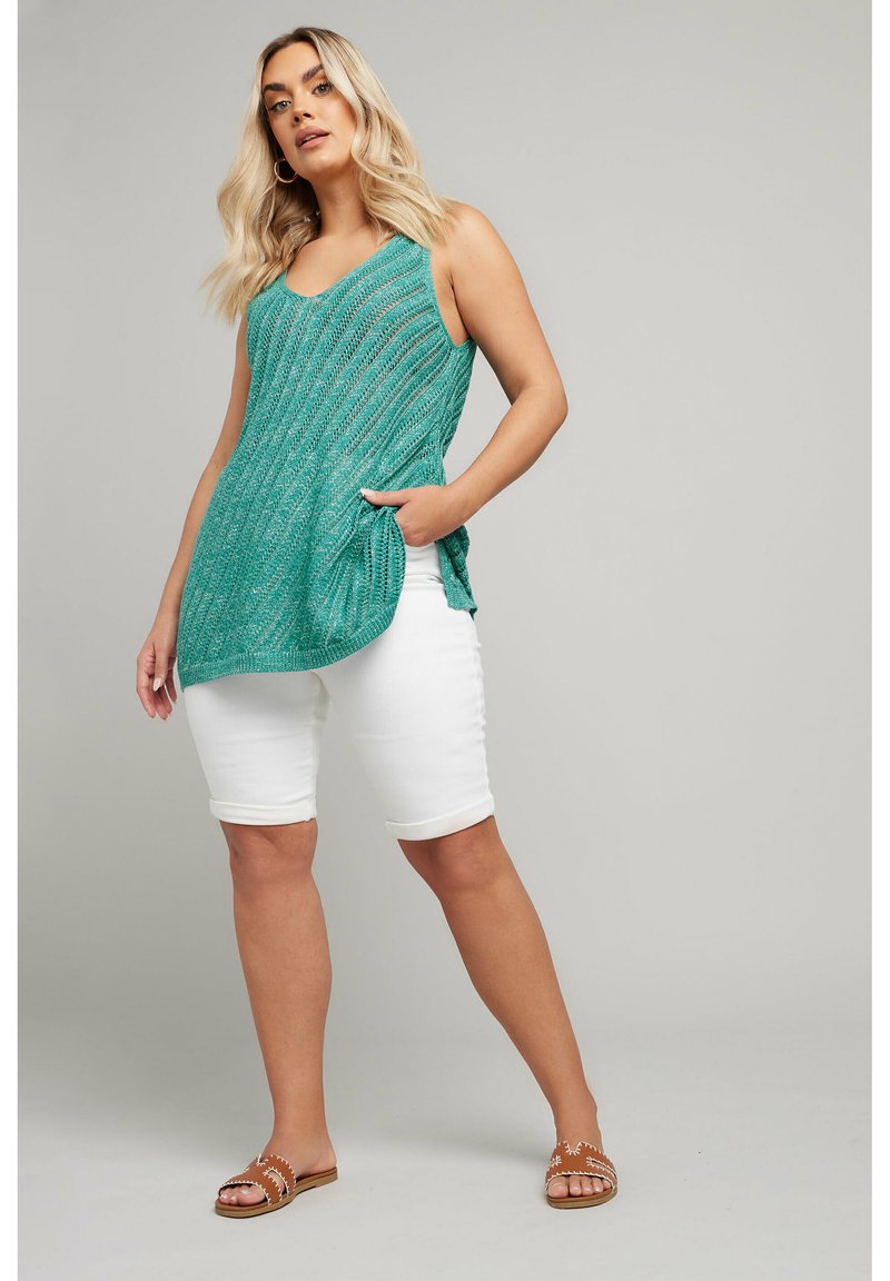 Teal stickad linne med V-ringning, med sid slits, parat med vita bermudashorts och bruna sandaler med dekorativa detaljer.