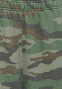 Taille élastique et tissu avec motif camouflage vert, marron et noir sur les vêtements.