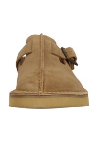 Wildleder Slipper in Tan mit einem breiten Riemen und Schnallen-Detail. Verfügt über eine abgerundete Zehenpartie und eine niedrige Gummisohle. Strukturierte Oberseite sorgt für Tiefe.