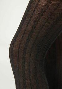 Sorte strømpebukser med mønster, der har teksturerede striber og kabel-strik design, hvilket skaber et semi-gennemsigtigt udseende med en glat finish.