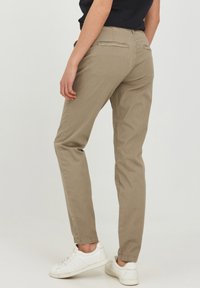 Pantaloni beige slim fit in un tessuto leggero con una texture liscia. Presentano tasche posteriori e orli a cuffia; abbinati a sneaker bianche.