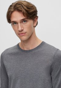 Grauer Pullover mit langen Ärmeln aus weichem Stoff und Rundhalsausschnitt. Verfügt über eine glatte Textur und eine figurbetonte Silhouette.