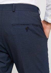 Donkerblauwe gestructureerde broek met een achterzak met knoopsluiting, een getailleerde pasvorm en een tailleband met riemlussen.