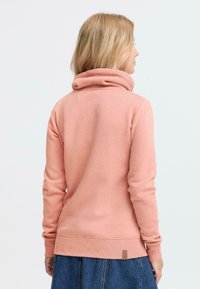 Felpa con cappuccio in un morbido rosa, caratterizzata da un colletto alto e polsini a coste. Il retro presenta una texture liscia e un piccolo tag con logo all'orlo.