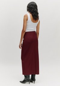 Bordeaux maxi rok van een zachte stof, met een getailleerde taille. Zwarte hakken voegen contrast toe, met daarboven een eenvoudig wit tanktop.