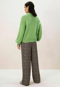 Pull vert surdimensionné avec mailles texturées, associé à un pantalon large imprimé léopard. L'ensemble présente une coupe décontractée et des matériaux doux.