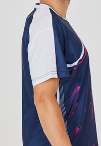 Marinblå sportströja med vita ärmar. Har en diagonalt rosa design och rena linjer. Materialet verkar lätt och mjukt.