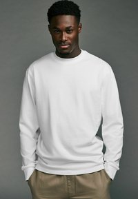 Witte langekousen overhemd met ronde hals, met een gladde textuur en een relaxed fit, gedragen met lichtgekleurde broeken.