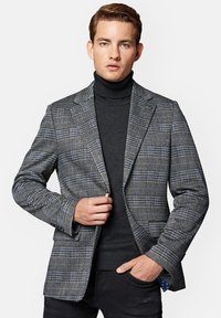 Szary marynarka w kratę, cechująca się dopasowanym krojem, klapami o wykroju typu notch oraz niebieskimi akcentami. Nosi się ją na czarnym swetrze z golfem z teksturowanej tkaniny.