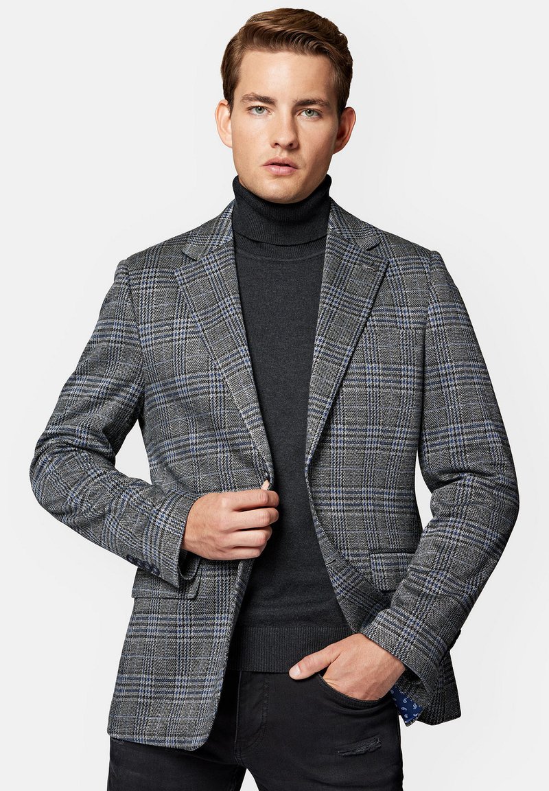 Szary marynarka w kratę, cechująca się dopasowanym krojem, klapami o wykroju typu notch oraz niebieskimi akcentami. Nosi się ją na czarnym swetrze z golfem z teksturowanej tkaniny.