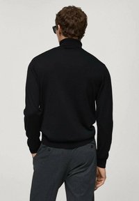 Schwarzer gestrickter Pullover mit hohem Kragen, langen Ärmeln und gerippten Bündchen, kombiniert mit dunkelgrauen Hosen mit Seitentaschen.