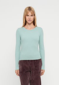 Μακρυμάνικο τοπ με ριγέ υφή σε ανοιχτό μέντα πράσινο, με στρογγυλή λαιμόκοψη. Το ύφασμα έχει ομαλή υφή. Φοριέται με φαρδιά, σκούρα μωβ παντελόνια.