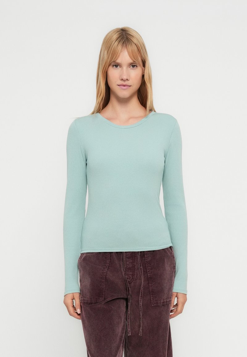 Μακρυμάνικο τοπ με ριγέ υφή σε ανοιχτό μέντα πράσινο, με στρογγυλή λαιμόκοψη. Το ύφασμα έχει ομαλή υφή. Φοριέται με φαρδιά, σκούρα μωβ παντελόνια.