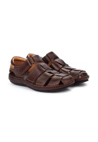 Braune Leder-Sandalen mit gewobenen Riemen, offener Zehenpartie, verstellbarem Klettverschluss und genähten Details entlang der Sohle.