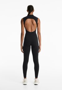 Zwarte sportieve jumpsuit met een hoge halslijn en een open rugontwerp; aansluitende body- en beensecties; gladde stof en slanke silhouet.