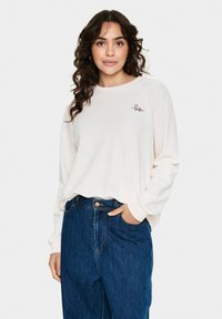 Chemise rose clair à manches longues avec un col rond et un motif brodé "love". Associée à un jean en denim bleu taille haute.