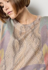 Lekki sweter z dzianiny w miękkim beżowym kolorze, z złotymi dekoracyjnymi ściegami i wielokolorowym abstrakcyjnym wzorem z falującymi kształtami.