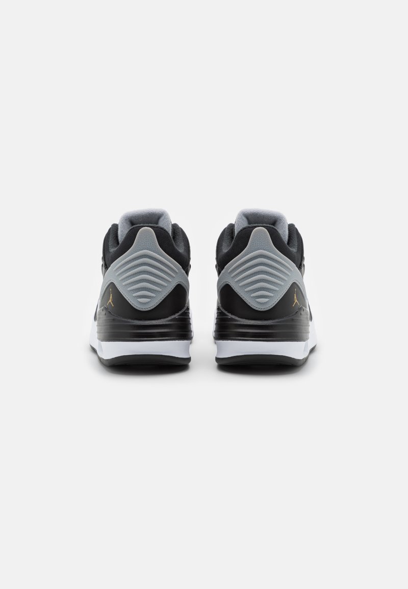 Schwarze und graue Sneakers mit glatter Oberfläche, gepolstertem Schaft, auffälliger strukturierter Ferse und weißer Sohle, die mit einem goldenen Logo-Element verziert ist.