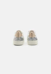 Ténis brancos com um calcanhar em glitter prateado texturizado, detalhes em pele castanha e um design de bico redondo. Estilo minimalista com sola plana.