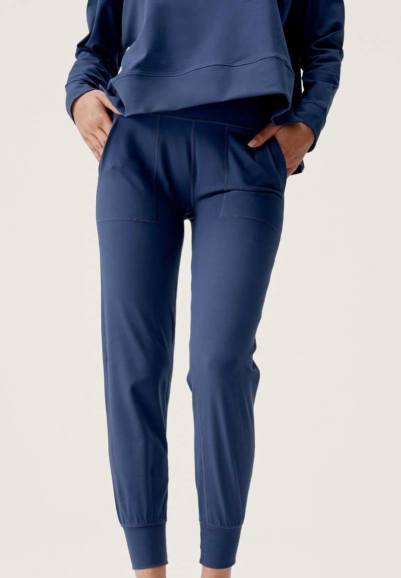 Jogging en bleu marine en tissu doux, avec deux poches avant et des poignets resserrés. Texture lisse avec des coutures contrastées.