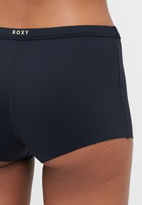 Marine svømmebukser laget av elastisk materiale, med en høy midje og Roxy-logo. Jevn tekstur og mid-høyde design.