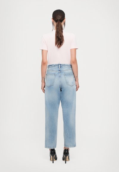 Light pink t-shirt paired with high-waisted light blue jeans. The jeans feature a relaxed fit and rear pockets, with pointed black heels.
