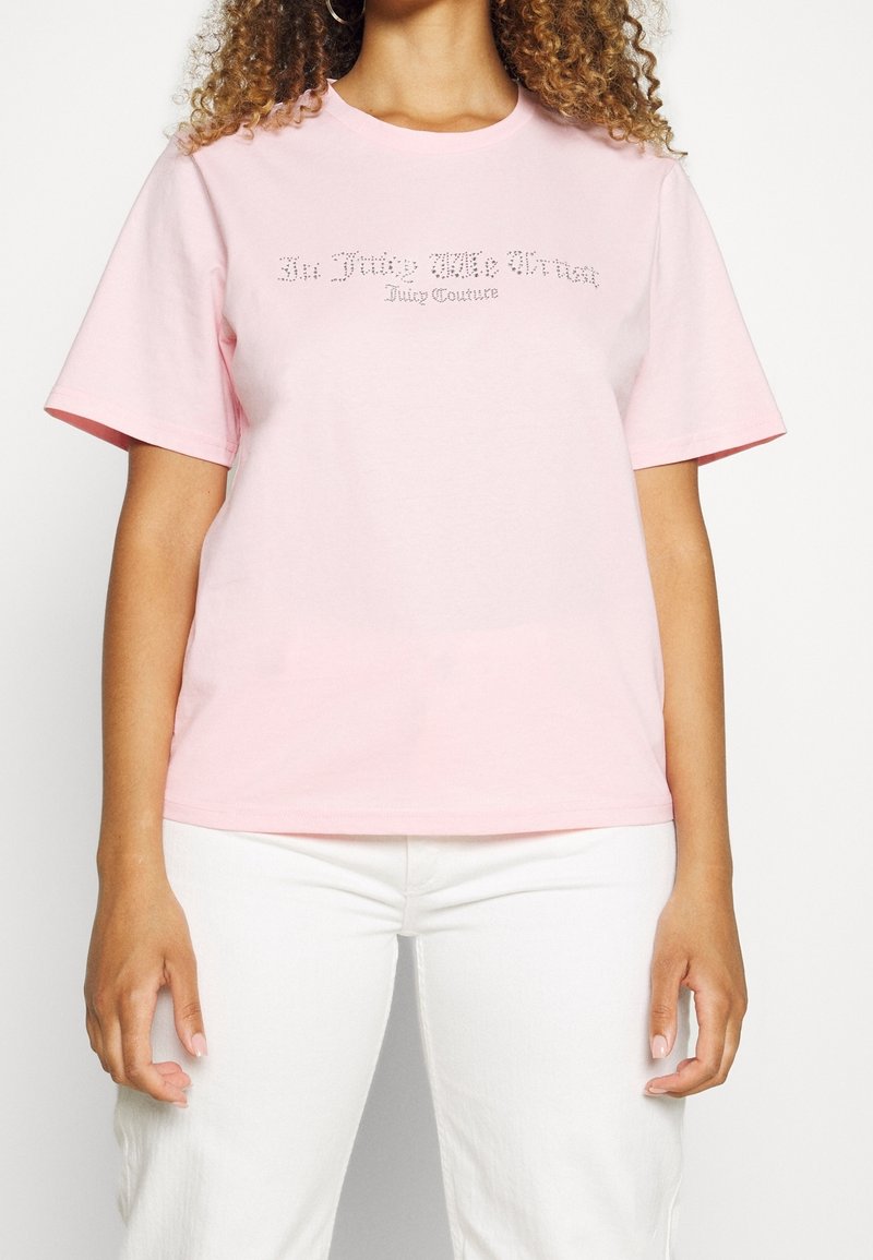 Světle růžové bavlněné tričko s krátkým rukávem, které na přední straně zdobí detail z kamenů s nápisem „In The Juice We Trust“.