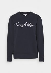 Donkerblauwe sweatshirt gemaakt van zachte stof met een ronde hals. Voorzien van een wit "Tommy Hilfiger" logo op de borst en geribbelde boordjes.