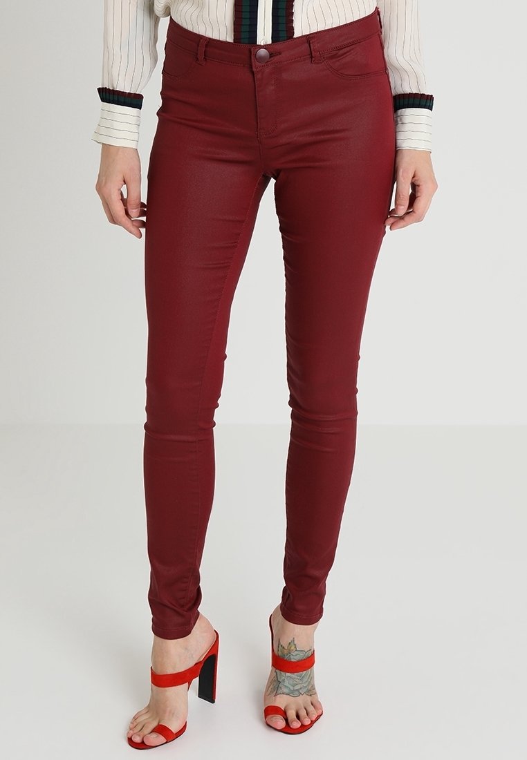 Jean skinny bordeaux avec une texture lisse et brillante, une ceinture avec fermeture par bouton et un design traditionnel à cinq poches.