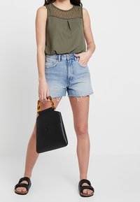 Haut sans manches vert olive avec des détails en maille, shorts en denim bleu clair, sac à main noir avec poignées en écaille de tortue, sandales noires.