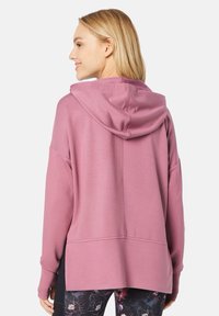 Rosa Kapuzenpulli mit lockerer Passform, ausgestattet mit einer Kordelzugkapuze, langen Ärmeln und einem leicht verlängerten Rückensaum. Weicher Stoff.