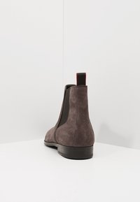 Botte Chelsea en daim marron avec des panneaux latéraux élastiques et un onglet de tirage rouge contrastant à l'arrière. Présente un bout arrondi élégant et une semelle plate.