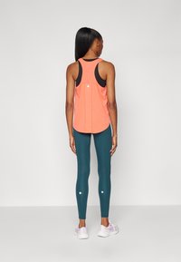 Koral atletisk singlet med racerback-design; turkise leggings med perforerte mønstre; hvite sneakers med subtil merkevare.