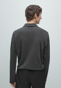 Donkergrijs poloshirt met lange mouwen, een zachte textuur en een klassieke kraag, gezien van achteren met een losse pasvorm.