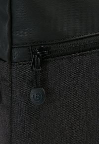 Borsa in tessuto nero con un aspetto tessuto e strutturato. Presenta una zip liscia e lucida e un bottone molle rotondo con un dettaglio del logo.