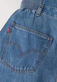 Заден джоб на сини дънки с оранжева нишка и малък червен етикет Levi's от лявата страна.