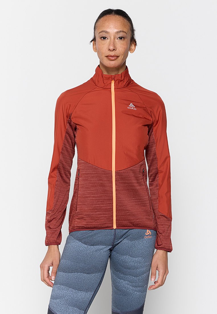 Rote und bordeauxfarbene Sportjacke mit durchgehendem Reißverschluss, hohem Kragen und kontrastierendem orangefarbenem Reißverschluss. Strukturierter Stoff an den Ärmeln, taillierte Passform.