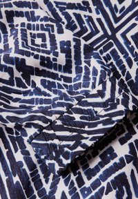 Modrý a námořnický geometrický vzorovaný textil, obsahující složité tvary a linie na bílém pozadí s hladkou texturou.