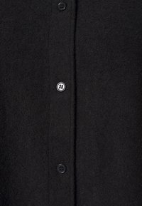 Chemise en polaire noire au toucher doux, dotée d'une fermeture à bouton sur le devant et de boutons noirs pour la fermeture. Design simple et minimal.