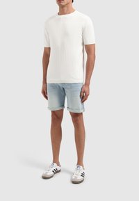 Witte ribbelige kortsleeve gebreide shirt, gecombineerd met lichtblauwe denimshorts met opgerolde zomen en witte sneakers met zwarte strepen.